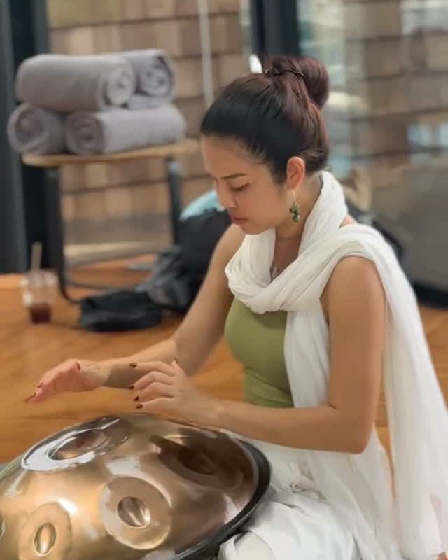 Kai playing the handpan inside the shala, rolled mats on the bench behind her